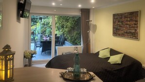 A bedroom with a bed, a TV mounted on the wall, and a view of an outdoor patio with a table and chairs.