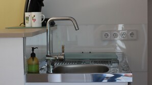 A kitchen sink with a faucet, a soap dispenser, and a mug with a floral design on a shelf above.