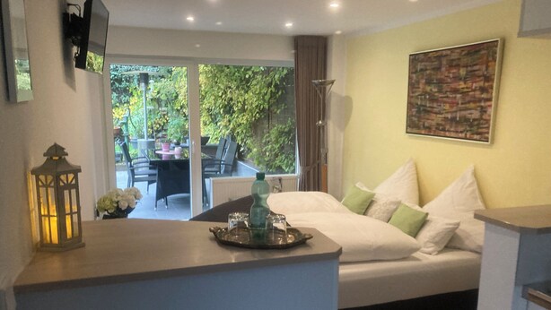 A bedroom with a bed, a nightstand, a lamp, and a view of an outdoor patio with a table and chairs.
