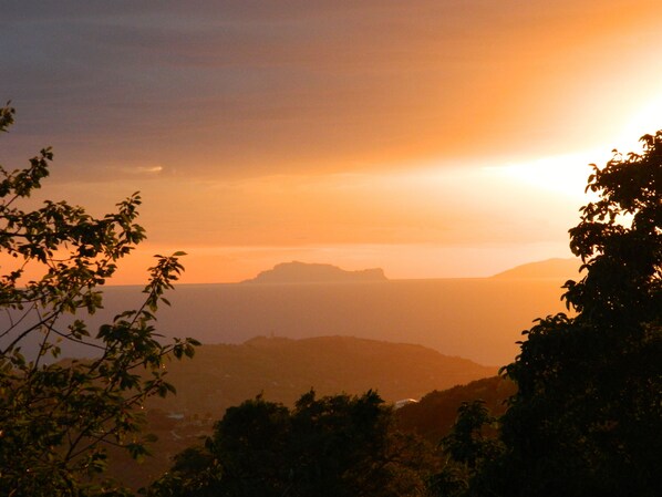 Une vue sur le coucher de soleil depuis un point de vue élevé, avec les silhouettes de collines et d’arbres au premier plan.