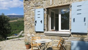 A stone building with a stone patio, a table with two chairs, a potted plant, and a view of the countryside. - Casa Mancose, vacation in the olive grove with sea views in the Cilento (Cicerale (SA))