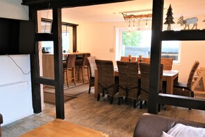 A dining area with wicker chairs and a wooden table, a black-framed window, and a ceiling light fixture.
