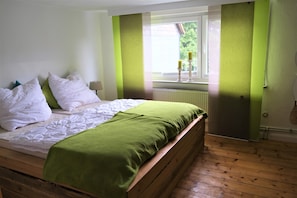 A bedroom with a wooden bed, white bedding, and green accents on the walls and curtains.