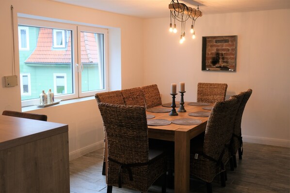 A dining area with a wooden table, wicker chairs, candles, and a view of buildings through a window.