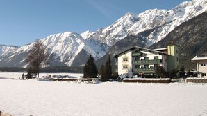 Un hotel dallo stile architettonico alpino tradizionale, con un balcone ben in vista e vista sulle montagne innevate.