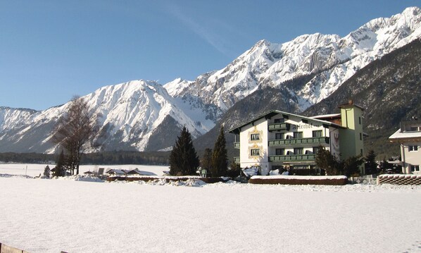 A hotel with a traditional Alpine architectural style, featuring a prominent balcony and a view of snow-covered mountains.