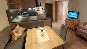 Un ambiente compatto con angolo cottura, zona pranzo completa di tavolo e sedie, divano, televisore e armadio.