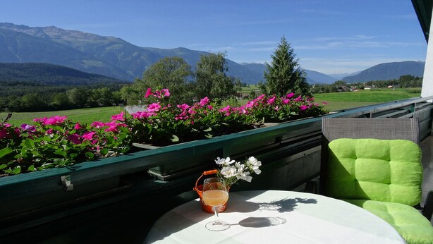 Un tavolo con un bicchiere e un fiore, con vista su un paesaggio montano.
