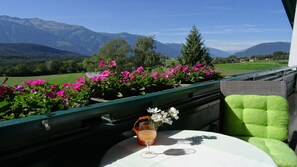 A table with a glass of drink and a flower, set against a scenic mountain view.