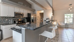 A modern kitchen with white cabinets, a granite countertop, stainless steel appliances, and a bar area with white chairs. - Contemporary Pool Villa I - just few minutes to Beach - heated Pool & Spa, WiFi! (VENICE)