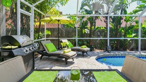 A covered patio area with a pool, lounge chairs, a grill, and a table with a drink. - Contemporary Pool Villa I - just few minutes to Beach - heated Pool & Spa, WiFi! (VENICE)