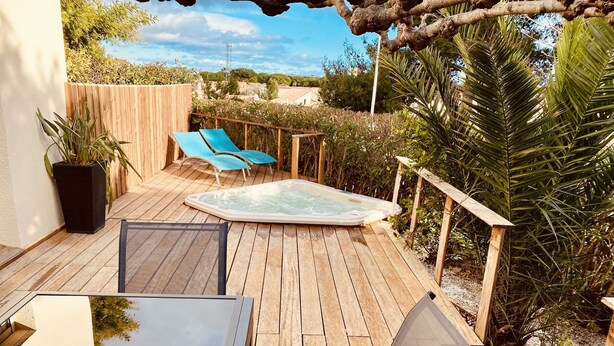 Una terraza de madera con un jacuzzi, dos sillones azules y una mesa con sillas.
