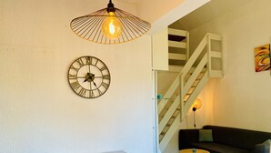 Una sala de estar con una mesa blanca, un reloj, una lámpara colgante, una escalera y un sofá.