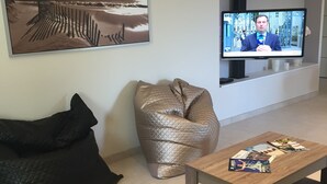 Un salon moderne doté d’un grand téléviseur à écran plat, d’un canapé beige, d’un fauteuil en forme de poire noir et d’une table basse sur laquelle sont posés des magazines.
