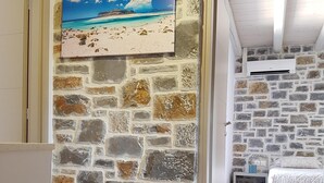 A room with a stone wall, a painting of a beach, a bed, and an air conditioning unit. - Charlise Luxury Villa by Cretevasion (Kokkini Hani)