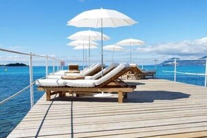 A wooden deck with lounge chairs and white umbrellas, overlooking a calm sea.