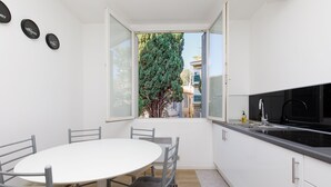 Una cucina compatta con zona pranzo, un'ampia finestra e vista su alberi e palazzi.