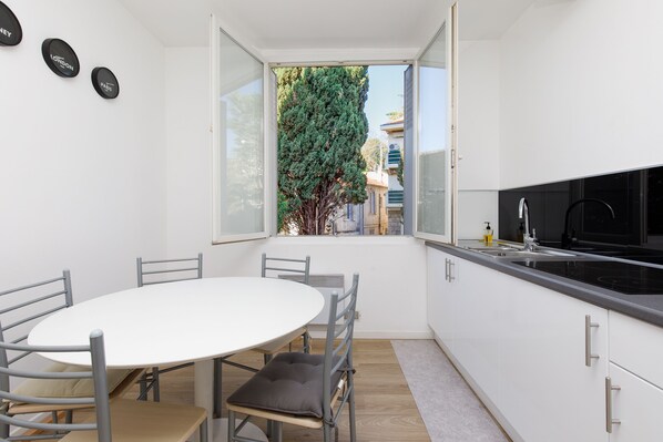A compact kitchen with a dining area, a large window, and a view of a tree and buildings outside.