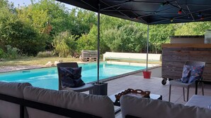A covered outdoor area with a pool, seating, and a wooden structure. - Air-conditioned villa with swimming pool in quiet village center with all amenities (Saint-Maurice-De-Gourdans)