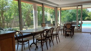 A spacious indoor area with large windows, a pool, and outdoor seating. - Air-conditioned villa with swimming pool in quiet village center with all amenities (Saint-Maurice-De-Gourdans)