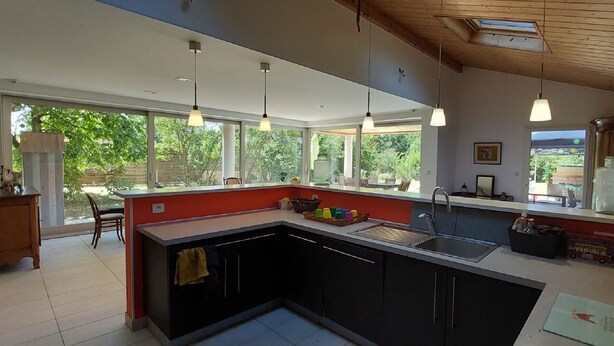 A modern kitchen with a large island, pendant lighting, and a view of the outdoors. - Air-conditioned villa with swimming pool in quiet village center with all amenities (Saint-Maurice-De-Gourdans)