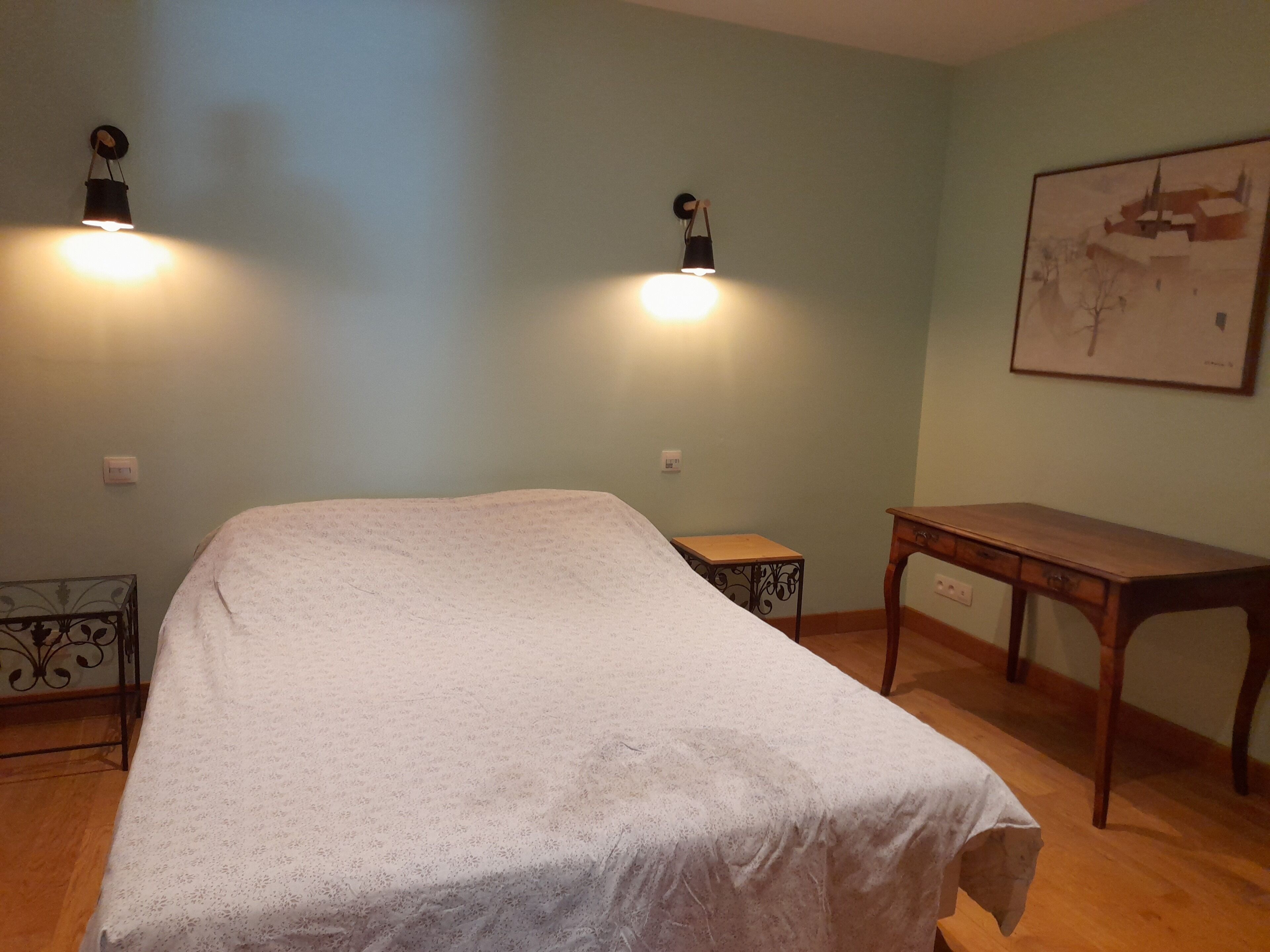 Une chambre à coucher avec un lit, deux lampes fixées au mur, une petite table et une table de chevet en bois.