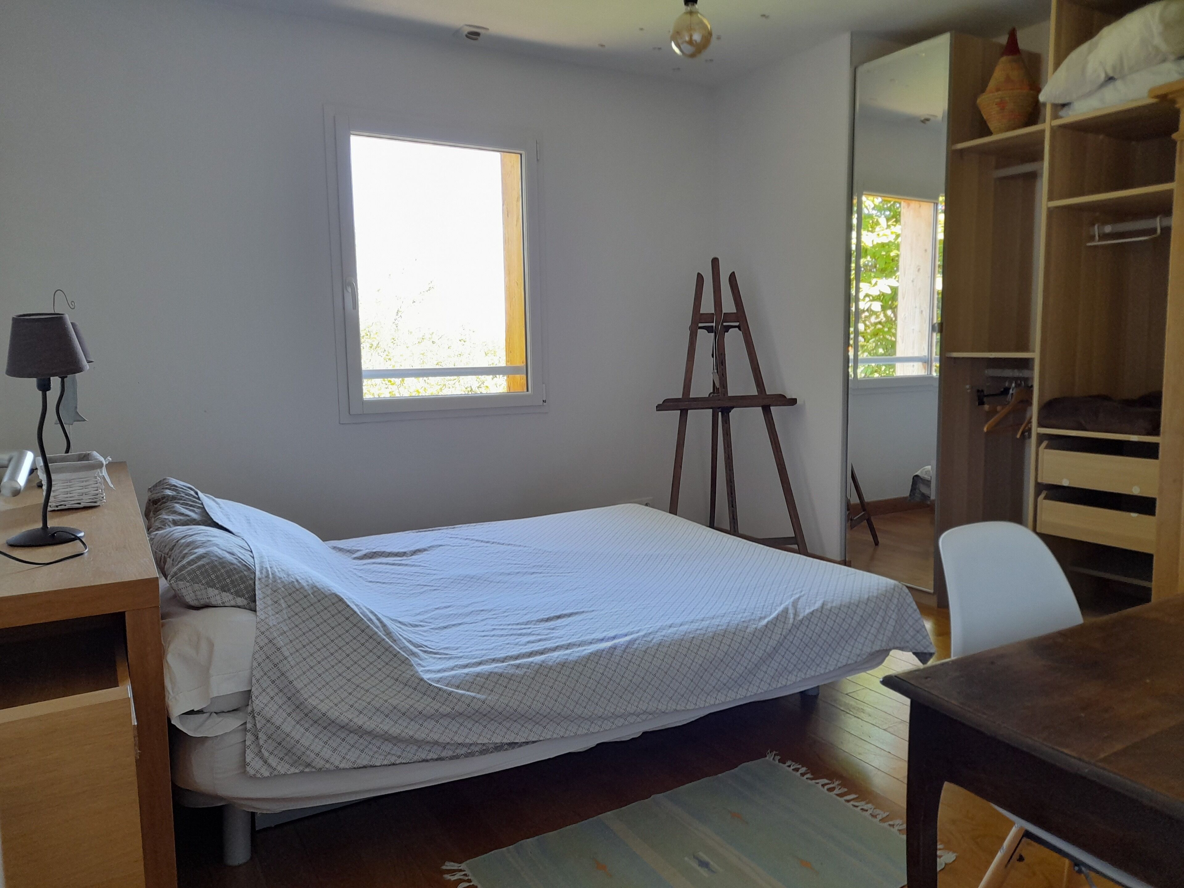 Een slaapkamer met een bed, een bureau, een lamp, een raam en een kledingkast.