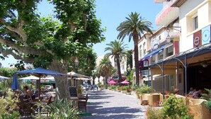 A sunny outdoor cafe with tables and chairs, surrounded by potted plants and umbrellas.