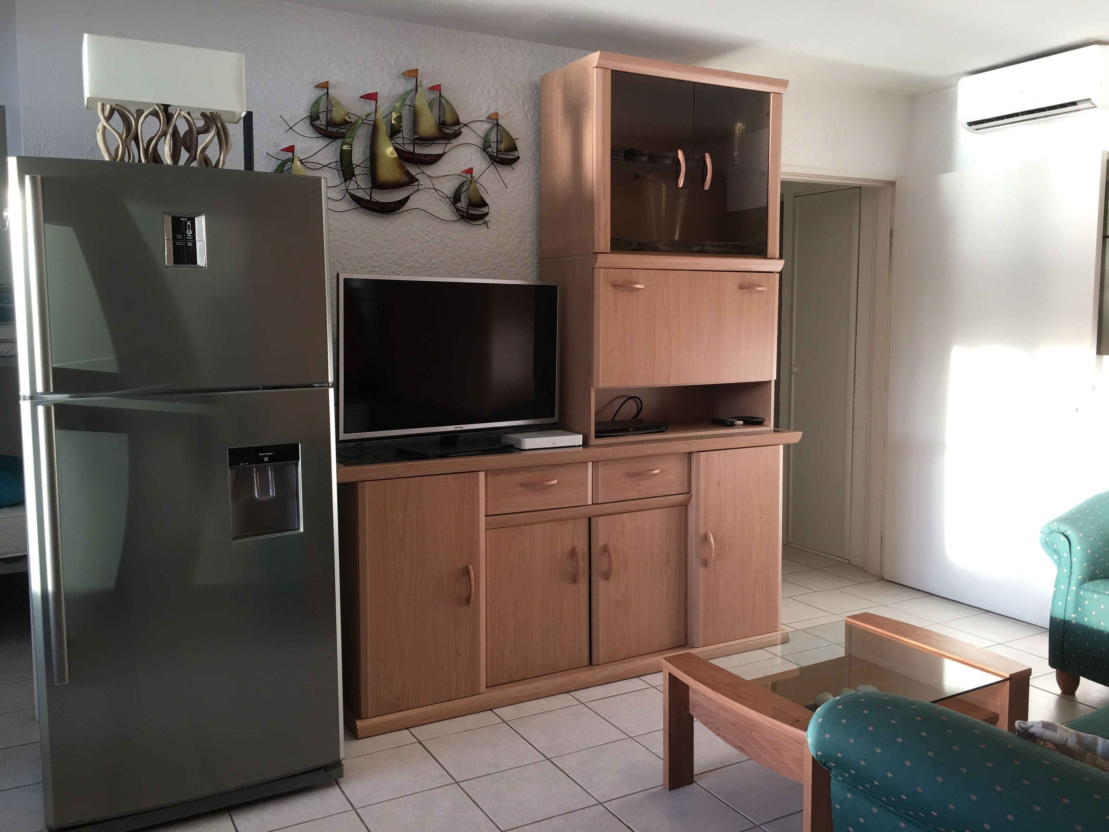 A compact living space with a built-in refrigerator, a wooden cabinet with a TV, and a small seating area.