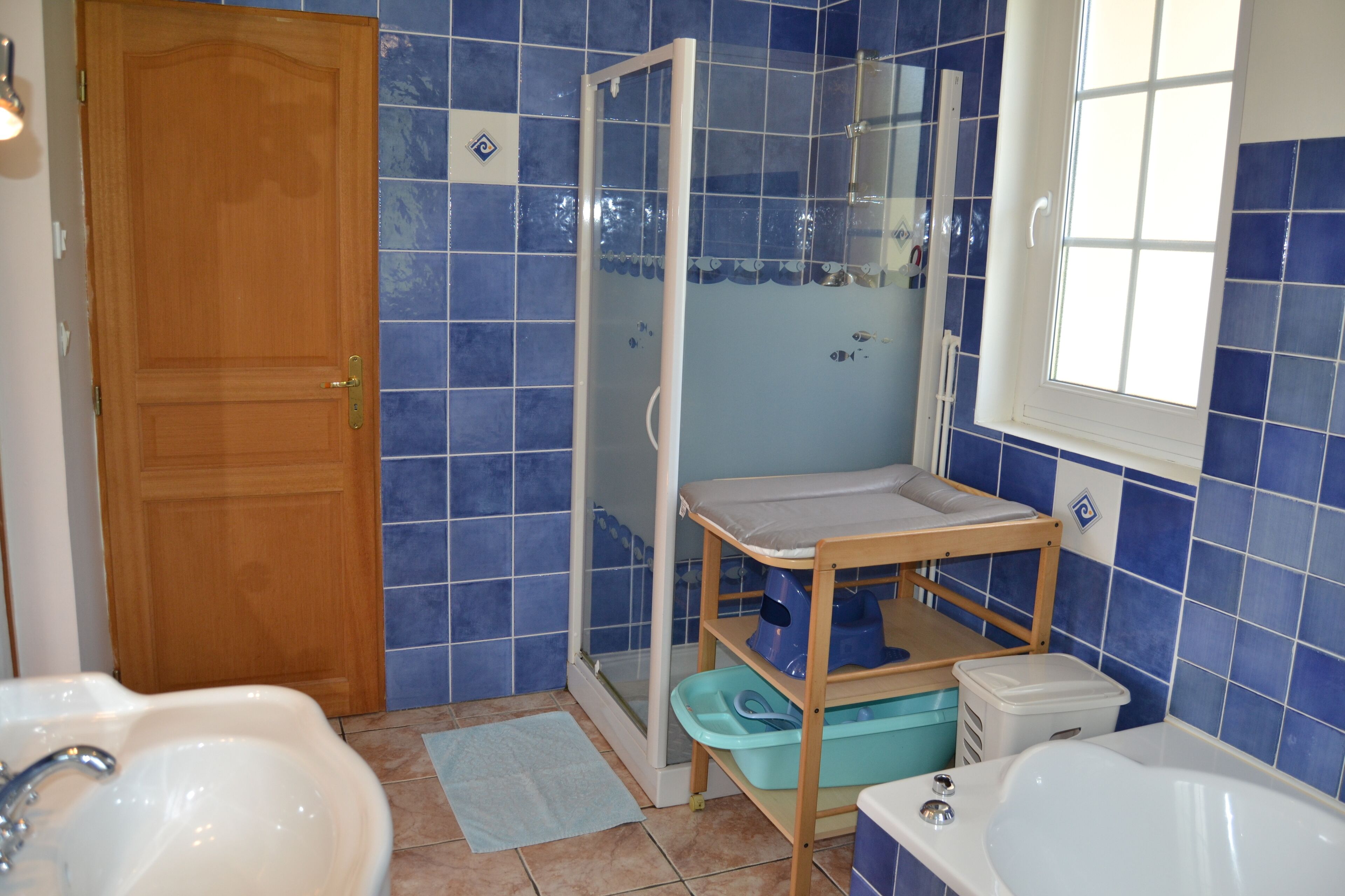 A bathroom with a wooden door, a shower enclosure, a sink, a bathtub, and a shelf with toiletries.