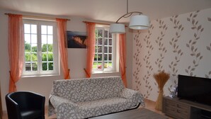 A living room with a sofa, a chair, a coffee table, a TV, and two windows with curtains. - Country house 3 * comfortable 20 minutes of Wi-7 pers- wonderful garden (Carville-Pot-De-Fer)