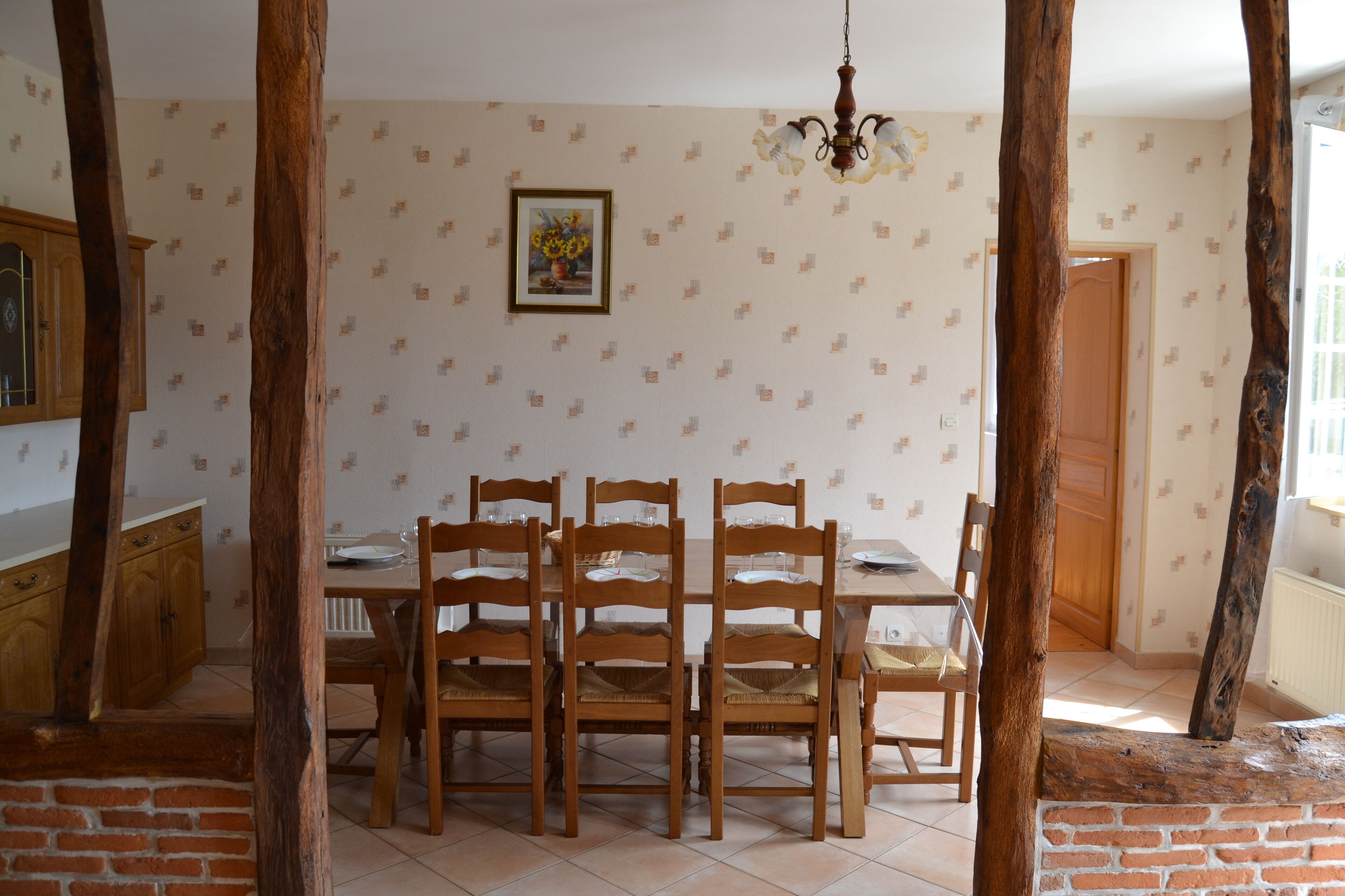 Comedor con mesa y sillas de madera, una araña y un papel tapiz estampado.