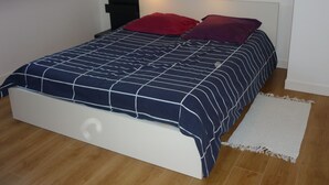 Een slaapkamer met een bed, nachtkastje, lamp en een wit tapijt.