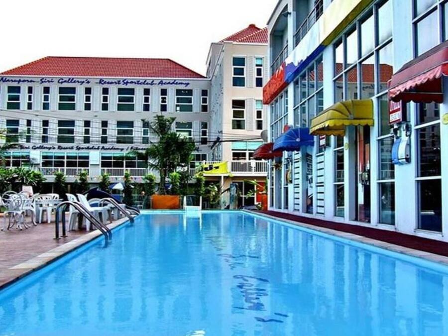 Una piscina con sillones de descanso y sombrillas, rodeada de edificios con señalización de un resort y un hotel.