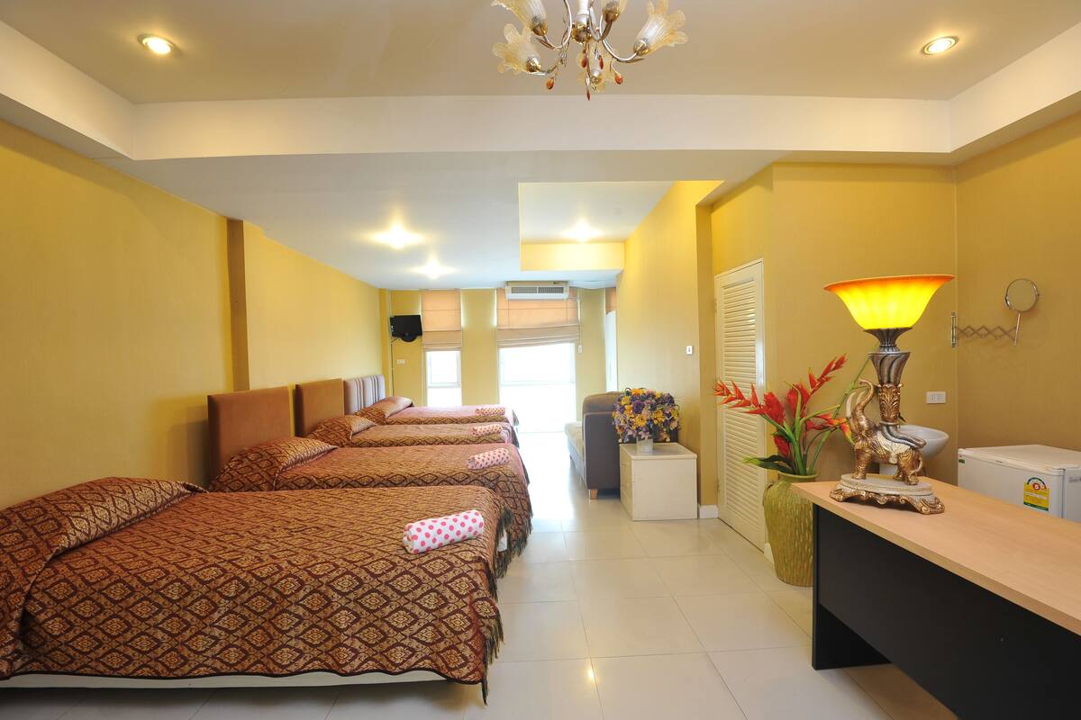 A hotel room with four beds, a desk, a lamp, and a small refrigerator.