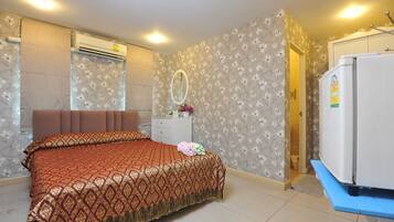 A bedroom with a bed, dresser, mirror, and a refrigerator.