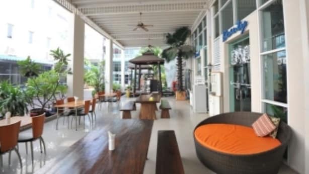 A covered outdoor seating area with tables and chairs, a central wooden bench, and a large wicker sofa with an orange cushion. - Nsiri Resort & Hotel (Lam Luk Ka)