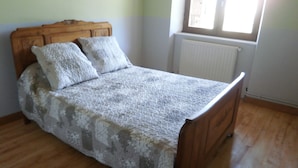 Un lit avec une tête de lit en bois et deux oreillers, un radiateur et une fenêtre laissant entrer la lumière naturelle.