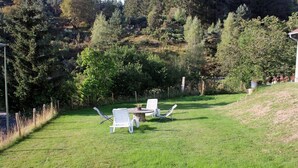 Un espace extérieur verdoyant avec une table en pierre et deux chaises blanches.