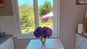 A kitchen with a window, a table with two benches, and a vase with purple flowers. - house near shops, small echo of the pond Mode 5 ha 15 minutes from the sea, hiking (Châtelaudren)