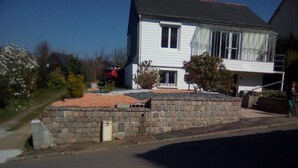 A two-story house with a stone wall in front, a small garden, and a clear sky. - house near shops, small echo of the pond Mode 5 ha 15 minutes from the sea, hiking (Châtelaudren)