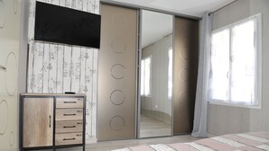 Un dormitorio con cama, armario con varios cajones, espejo y puerta corredera que da a otra habitación.