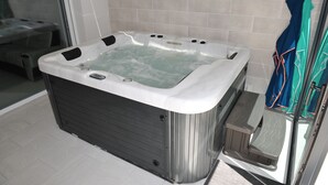 Un baño moderno con una bañera de hidromasaje grande y cuadrada, un box de ducha con mampara de vidrio y un perchero con toallas a la vista.