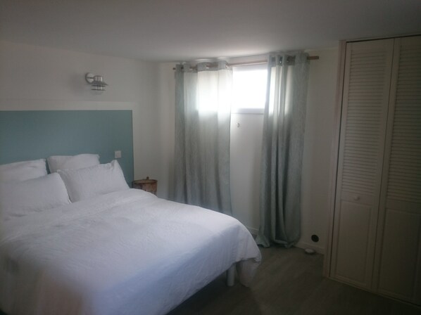 A bedroom with a bed, a nightstand, a window with curtains, and a wardrobe. - Rental charming T2 Vendée 300m from the beach and 100 m from the forest (Saint-Jean-De-Monts)
