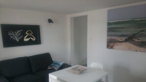 A modern living room with a black sofa, a white table, and a painting of a beach scene. - Rental charming T2 Vendée 300m from the beach and 100 m from the forest (Saint-Jean-De-Monts)