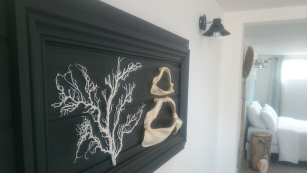A room with a black-framed artwork of a tree and two animal skulls, a bed with white bedding, and a wooden stool. - Rental charming T2 Vendée 300m from the beach and 100 m from the forest (Saint-Jean-De-Monts)