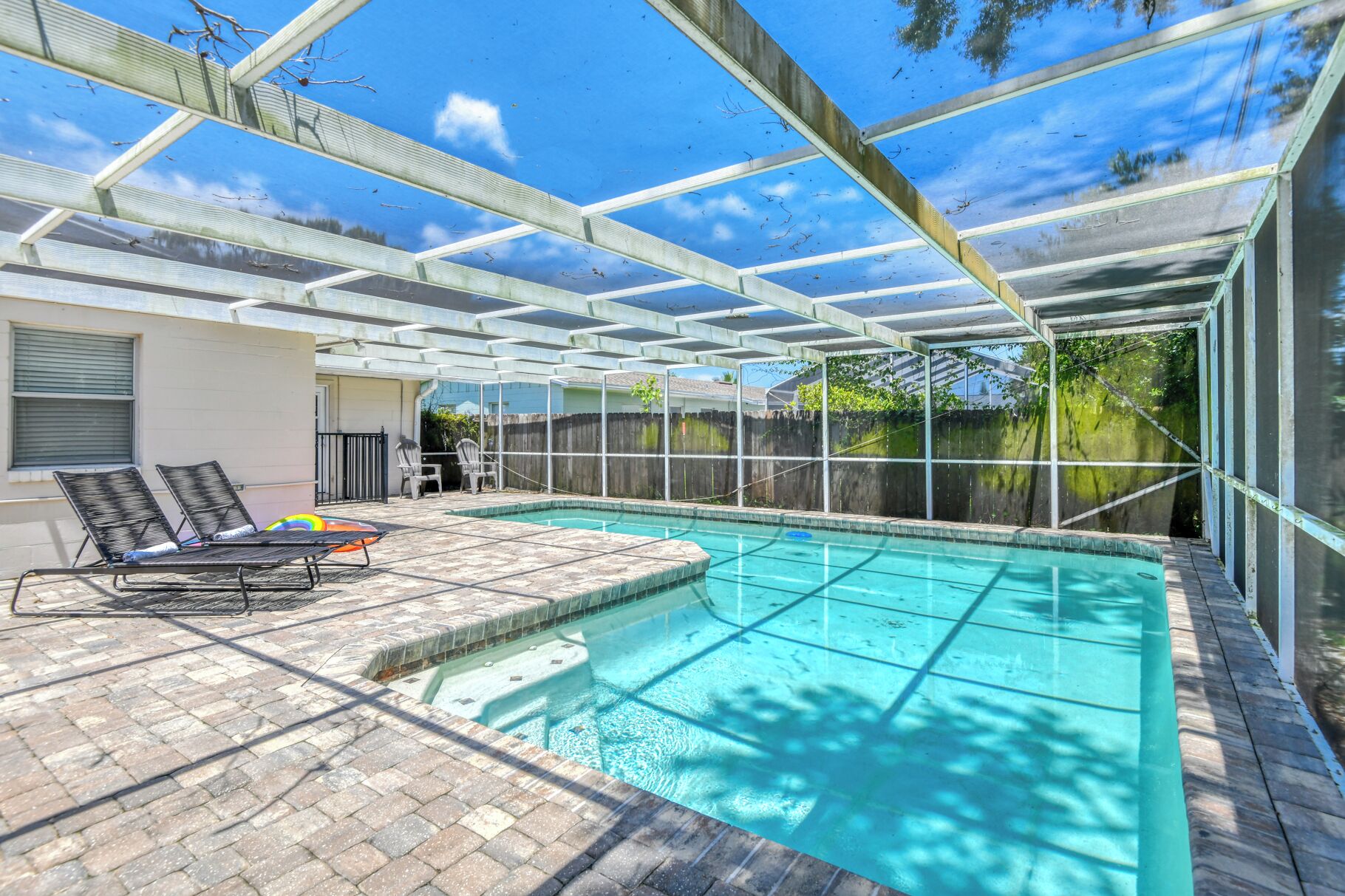 A covered outdoor swimming pool with a patio area, including lounge chairs and a small table.