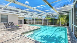 A covered outdoor swimming pool with a patio area, including lounge chairs and a small table.