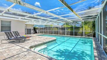 A covered outdoor swimming pool with a patio area, including lounge chairs and a small table.