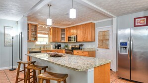 A kitchen with wooden cabinets, a granite countertop, a stainless steel refrigerator, and a coffee maker.